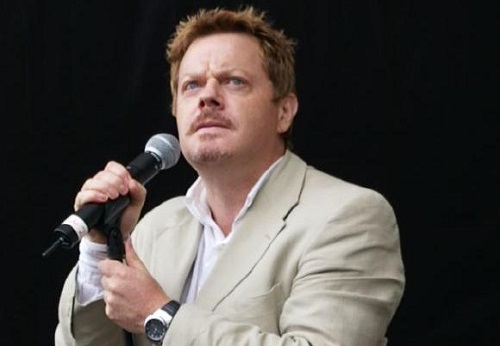 Eddie Izzard holding a mic and looking upward