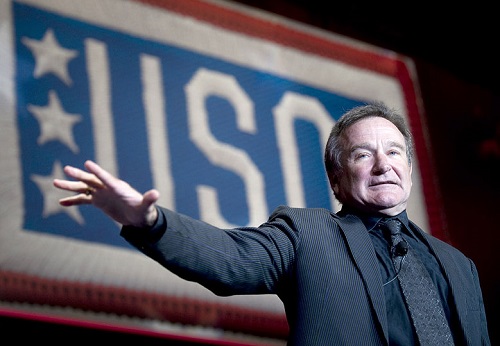 Robin Williams spread his right arm open in front of a USD backdrop